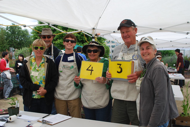 Image of group of volunteers at a UC Davis Arboretum plant sale. They are smiling, wearing aprons and holding numbers